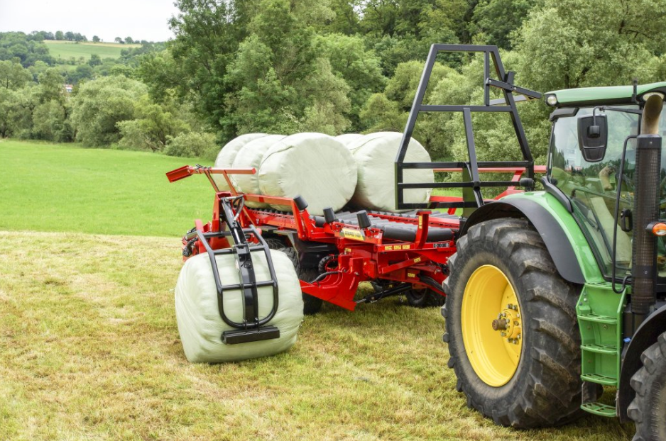 Anderson RBMPRO 1400 bale gripper lifting a wrapped round bale beside the trailer