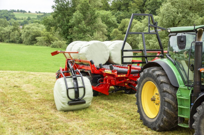 Anderson RBMPRO 1400 bale gripper lifting a wrapped round bale beside the trailer