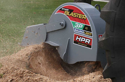 Closer view of the Baumalight 3P40 cutter housing grinding a stump beside a tractor tire