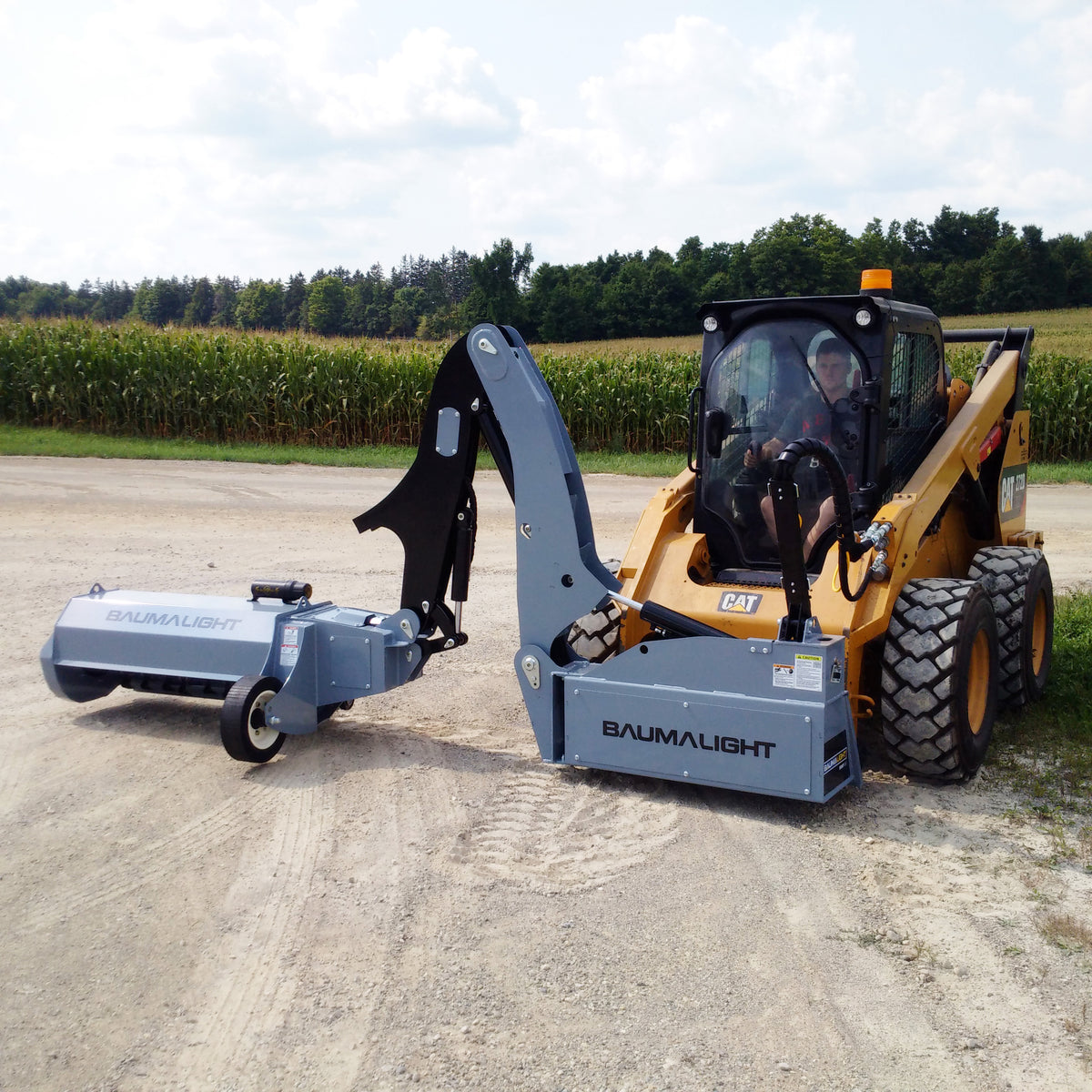 Baumalight SWF580 boom-and-stick mower with head supported at ground level beside a skid steer